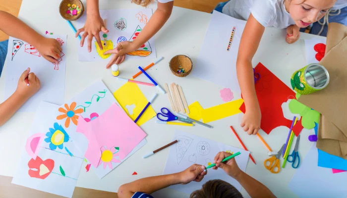 Enfants réalisant un atelier d'éveil créatif autour d'une table couverte de papiers colorés